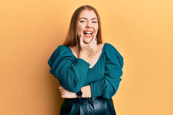 Young beautiful redhead woman wearing elegant and sexy look looking confident at the camera smiling with crossed arms and hand raised on chin. thinking positive.