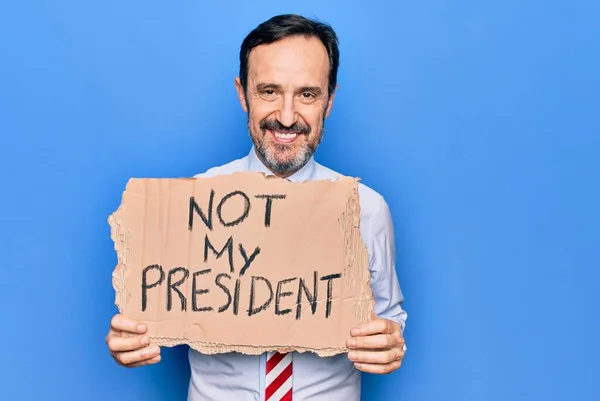 Middle age business man asking for political holding banner with not my president message looking positive and happy standing and smiling with a confident smile showing teeth