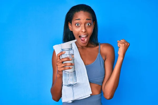 身穿运动服的年轻的非洲女人喝着一瓶水 自豪地尖叫着 高举双臂庆祝胜利和成功 — 图库照片