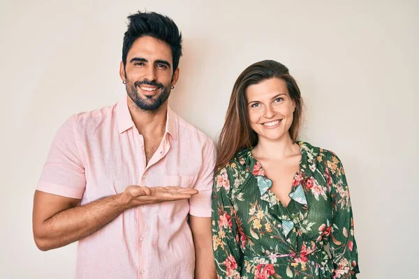 Güzel, genç bir çift sevgili birlikte gülümsüyor. Neşeli bir şekilde sunuyor ve avuç içiyle kameraya bakıyor.. 