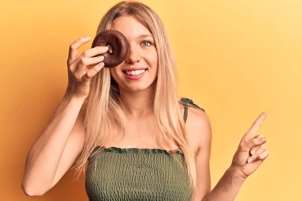 Mladá Blondýna Žena Drží Koblihu Úsměvem Šťastný Ukazující Rukou Prstem — Stock fotografie