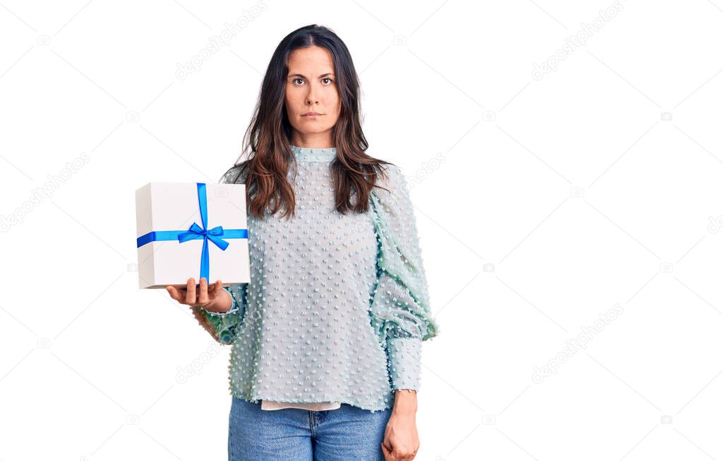 Young beautiful brunette woman holding birthday gift thinking attitude and sober expression looking self confident 