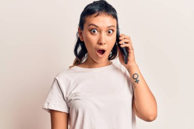 Akıllı telefonda konuşan genç bir kadın korkmuş ve şaşırmış bir şekilde ağzı açık kalmış, inançsız bir yüz. 