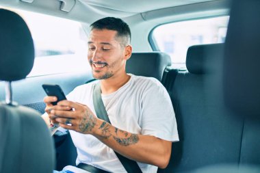 Genç İspanyol adam mutlu bir şekilde gülümsüyor. Arabada otururken akıllı telefon kullanıyor..