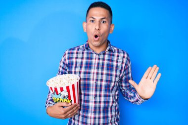 Patlamış mısırı elinde tutan genç, yakışıklı Latin bir adam. Korkmuş ve ağzı açık kalmış, şaşırmış ve şaşırmış. 