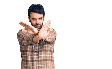 Gündelik kıyafetler giyen genç İspanyol adam. Reddedilmiş yüz ifadesi. Kollar ve avuçlar çapraz. 