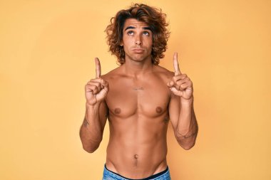 Genç İspanyol adam üstsüz dikiliyor üzgün ve üzgün görünüyor, parmaklarıyla yön gösteriyor, mutsuz ve depresif.. 