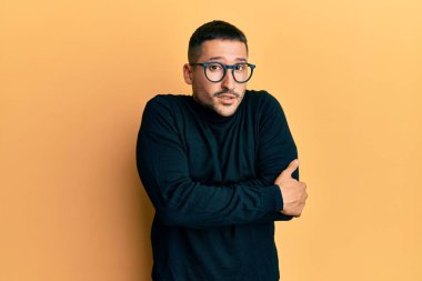 Balıkçı yaka kazak ve gözlük takan yakışıklı bir adam. Kış soğuğu için titriyor ve donuyor. Yüzünde üzgün ve şok ifadesi var. 