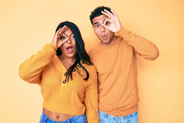 Güzel, Latin, genç bir çift, günlük kıyafetlerini giyip, şaşırmış yüz ifadesiyle, parmaklarının arasından bakarak hareket ediyorlar. İnançsız ifade. 