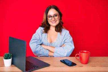 Ofiste çalışan, dizüstü bilgisayarlı, mutlu yüzlü, kollarını kavuşturup kameraya bakan güzel beyaz bir kadın. pozitif kişi. 