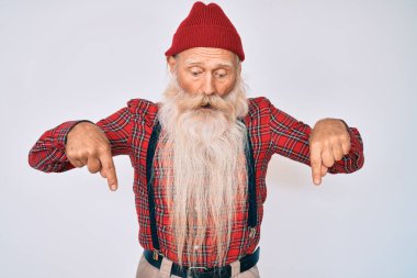 Gri saçlı ve uzun sakallı yaşlı bir adam. Hipster görünümlü, yün şapkalı, parmakları reklamını gösteren, şaşırmış yüzlü ve ağzı açık biri. 