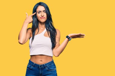 Güzel İspanyol kadın gündelik giysiler giyiyor. Kafası karışmış ve avuç içi açık fotokopi alanı göstermekten rahatsız olmuş ve alnını işaret ediyor. Bunu bir düşün.. 