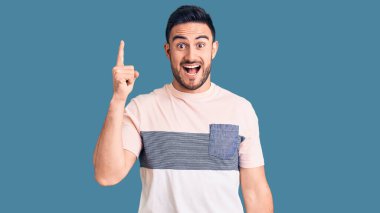 Gündelik giysiler giymiş genç yakışıklı bir adam başarılı bir fikri işaret ediyor. Heyecanlı ve mutlu. Bir numara.. 