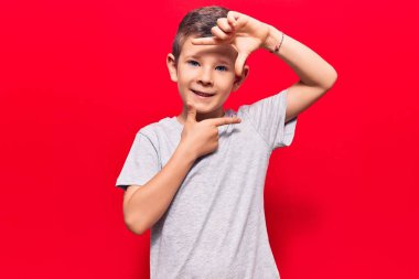 Gündelik kıyafetler giyen sevimli sarışın çocuk gülümseyerek elleri ve parmakları gülen yüzüyle çerçeve yapıyor. yaratıcılık ve fotoğrafçılık kavramı. 