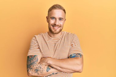 Sıradan çizgili tişört giyen, kollarını kavuşturup kameraya gülümseyen beyaz bir genç. pozitif kişi. 