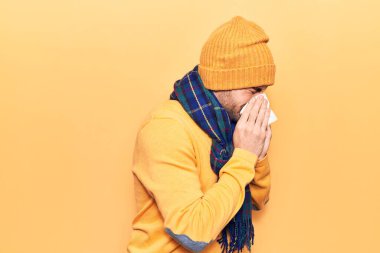 Burun üstü kağıt mendil kullanan genç adam hastalığı. Sarı arka plan üzerinde eşarp ve yün şapka takıyor.