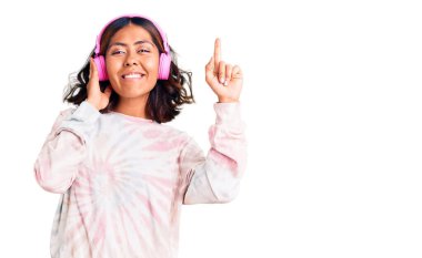 Genç, güzel, melez, müzik dinleyen, kulaklık takan bir kadın bir fikir ya da soruyla şaşırmış, mutlu yüzle işaret eden bir numara. 