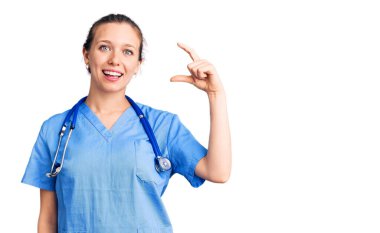 Genç, sarışın, doktor üniforması giyen, steteskop takan, gülümseyen, kendine güvenen, el hareketi yapan, parmakları küçük gösteren ve kameraya bakan güzel bir kadın. ölçüm kavramı. 