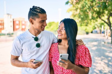 Şehrin caddesinde akıllı telefon kullanarak mutlu bir şekilde gülümseyen genç Latin çift..
