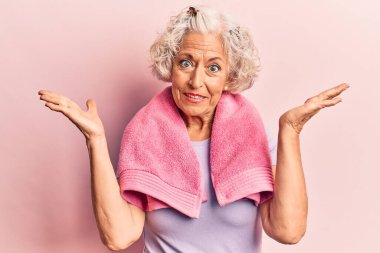 Kıdemli gri saçlı kadın spor giysisi ve havlu giyiyor, habersiz ve kolları açık, hiçbir fikrim yok ve şüpheli bir yüz var.. 