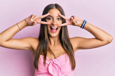 Kolsuz tişörtlü, sıradan giyinen genç İspanyol kadın barış sembolü yapıyor. Yüzünde parmaklar, gülümseyerek zaferi gösteriyor. 