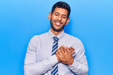 İş kıyafetleri giymiş, göğsünde elleri kapalı, yüzünde minnet ifadesi olan genç Latin bir adam. sağlık kavramı. 