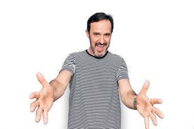 Orta yaşlı, çizgili tişört giyen yakışıklı adam izole edilmiş beyaz arka planda dikilip kameraya sarılmak için gülümseyerek bakıyor. Mutluluğu kucaklayan neşeli bir ifade..