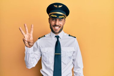 Yakışıklı İspanyol pilot üniforması giyen üç numarayı gösterip işaret eden kendinden emin ve mutlu gülümseyen adam.. 