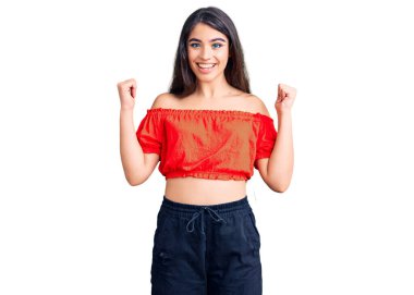 Esmer genç kız gündelik giysiler giyip şaşkınlık ve şaşkınlık içinde kolları açık ve gözleri açık bir şekilde başarıyı kutluyor. Kazanan konsept. 