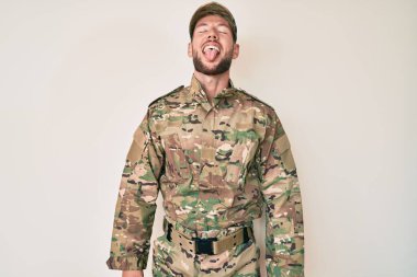 Kamuflaj üniforması giyen genç beyaz adam komik bir ifadeyle dilini dışarı çıkarıyor. duygu kavramı. 