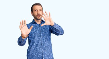 Sıradan kıyafetler giyen genç yakışıklı adam korku ifadesinden korkmuş ve dehşete düşmüş. El hareketlerini durdur, şok içinde bağır. panik konsepti. 