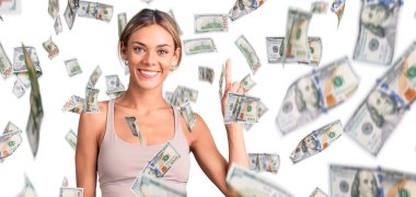 Güzel beyaz kadın spor giysisi giyer ve bir numaralı parmağını göstererek gülümserken kendinden emin ve mutlu..