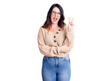 Güzel, genç, esmer bir kadın, günlük kıyafetler ve gözlük takıyor, gülümsüyor, kameraya göz kırpıyor ve parmaklarıyla zafer işareti yapıyor. İki numara.. 