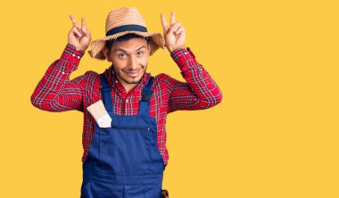 Yakışıklı Latin Amerikalı, tamirci üniforması giyen komik ve deli pozu veren, parmakları tavşan kulaklı, neşeli gülümseyen. 