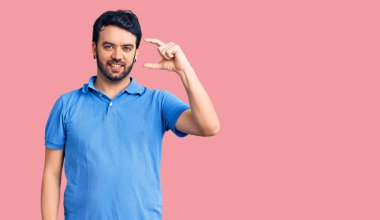 Gündelik kıyafetler giyen, gülümseyen, kendine güvenen, el hareketi yapan, parmaklarıyla işaret yapan ve kameraya bakan genç İspanyol bir adam. ölçüm kavramı. 