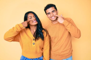 Güzel Latin bir çift, gündelik giysiler giyip el ve burunlarını göstererek neşeli bir şekilde gülümsüyor. güzellik konsepti 