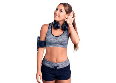 Spor kıyafetleri giyen, kulaklık takan, ağzı kulaklarında gülümseyen dedikoduları ve dedikoduları dinleyen genç ve güzel bir İspanyol kadın. Sağırlık kavramı. 