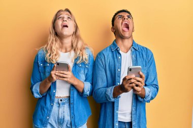 Irklar arası genç çift akıllı telefon kullanıyor kızgın ve kızgın çığlıklar sinirli ve öfkeli, öfkeyle bağırıyorlar.. 