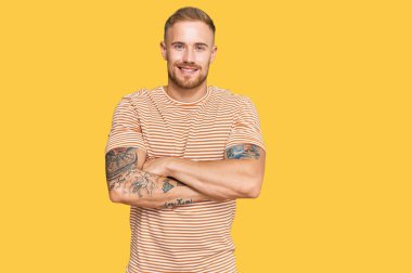 Sıradan kıyafetler giyen genç İrlandalı adam kollarını kavuşturup kameraya bakarken gülümsüyor. pozitif kişi. 