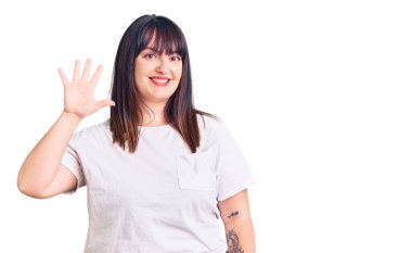 Genç ve cüsseli kadın gündelik kıyafetler giyer ve beş numarayı göstererek gülümserken kendinden emin ve mutlu görünürdü.. 