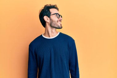 Gündelik kıyafetler ve gözlük takan genç İspanyol adam yüzünde gülümsemeyle yan yana bakıyor, doğal bir ifade. Kendinden emin gülen. 