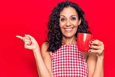 Orta yaşlı güzel bir kadın bir kupa kahve içiyor gülümsüyor mutlu bir şekilde elini ve parmağını yana uzatıyordu. 