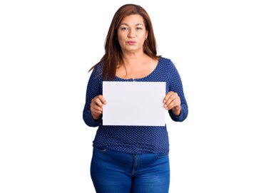 Orta yaşlı Latin kadın elinde kağıt pankartla boş alan düşünce tarzı ve ayık yüz ifadesi olan kendine güvenen bir kadın. 