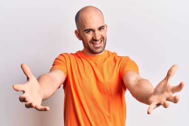 Genç, yakışıklı, kel bir adam, sıradan bir tişört giymiş kameraya bakıyor ve sarılmak için kollarını açmış gülümsüyor. Mutluluğu kucaklayan neşeli bir ifade.. 