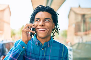 Genç Afrikalı Amerikalı gülümseyen mutlu bir adam şehrin caddesinde akıllı telefondan konuşuyor..