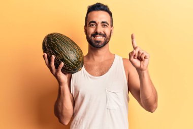 Elinde kavun tutan genç İspanyol bir adam bir fikirle gülümsüyor ya da bir soru işareti yapıyor mutlu bir yüzle, bir numara 