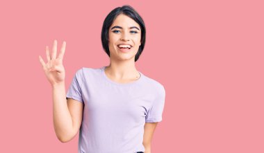 Esmer genç kız gündelik giysiler giyer ve parmaklarını dört numara ile gösterir ve gösterirken kendinden emin ve mutlu gülümserdi.. 