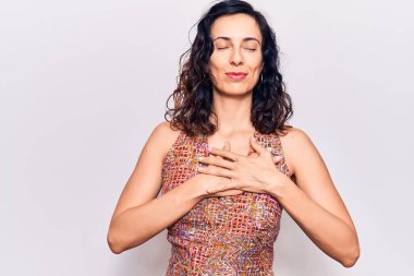 Gündelik kıyafetler giyen, göğsünde elleri, yüzünde minnet dolu bir jestle gülümseyen genç ve güzel bir İspanyol kadın. sağlık kavramı. 