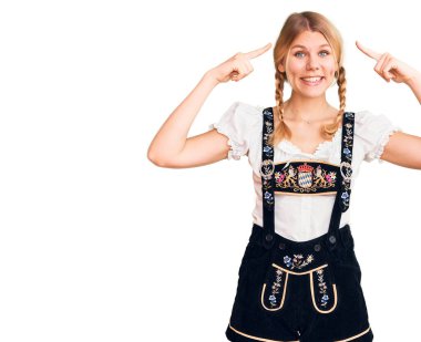 Oktoberfest elbisesi giyen genç güzel sarışın kadın iki eliyle başını gösteren gülümseme, harika bir fikir ya da düşünce, iyi bir hafıza. 