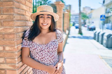 Tatildeki genç Latin kadın gülümsüyor. Şehrin duvarına yaslanmaktan mutlu..